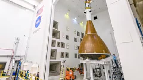 Orion spacecraft moving through large doorway into environmental test chamber facility