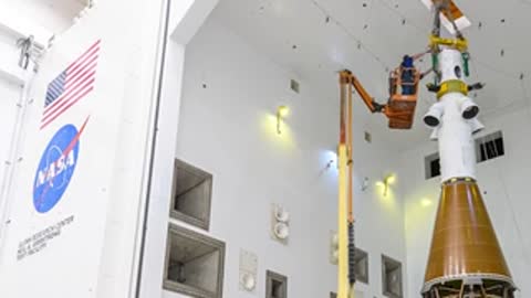 Technicians working around upper stage of spacecraft inside acoustic test facility