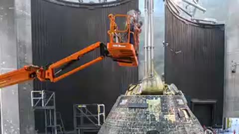 Technicians using lift equipment to inspect the top of the Orion capsule.