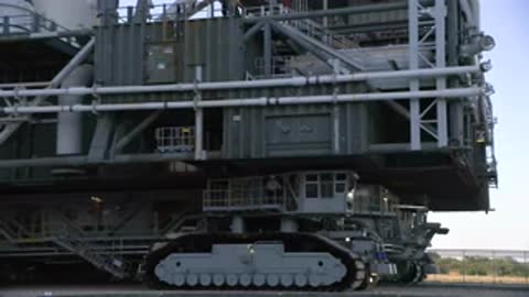 Close-up tracking shot of crawler transporter treads moving on road.