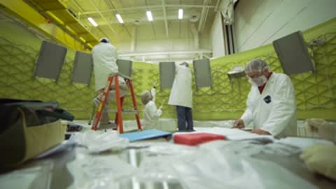 Technicians working along a large curved panel structure in a workshop.