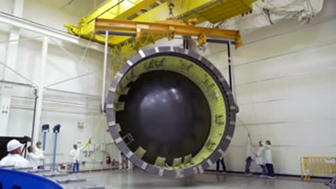 Engineers crane-lifting a large rocket stage section inside a high-bay facility.