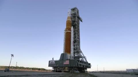 Static wide shot of SLS on crawler-transporter moving toward pad.