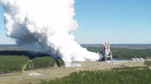A massive rocket engine test firing, producing large plumes of white smoke outdoors.
