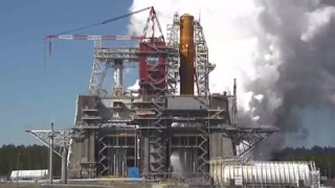 Rocket core stage test firing inside a large structural test stand framework.