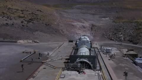 A horizontal rocket booster test firing in a desert canyon environment.