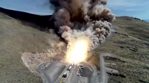 A rocket booster test fire generating intense bright flames and a large smoke plume in a canyon.