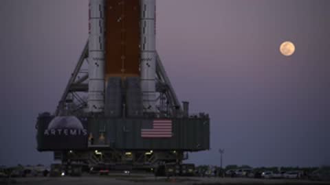 Static medium shot of SLS rocket with full moon in sky.