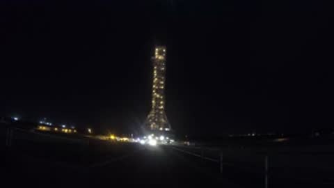 Nighttime shot of illuminated SLS rocket on crawler transporter during transit.