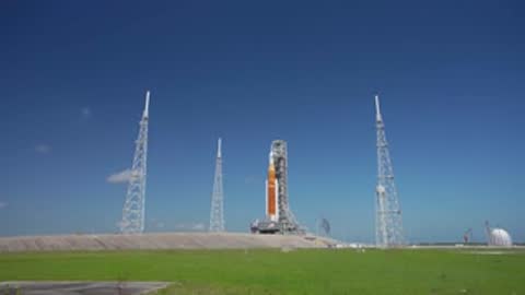 Wide static shot of SLS on launch pad under clear blue sky.