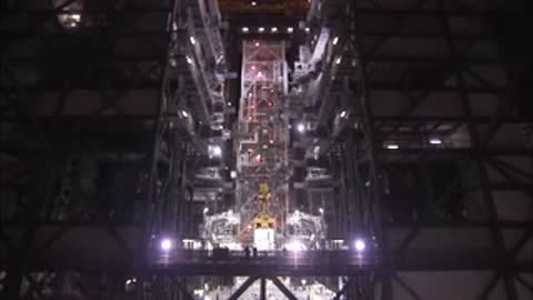 Looking down at workers on platforms inside the Vehicle Assembly Building around a central structure.