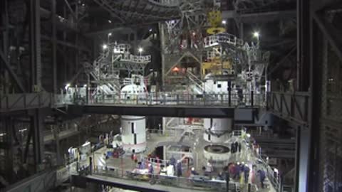 Medium view of technicians on multiple platforms inside the Vehicle Assembly Building with rocket sections.