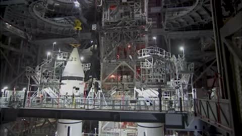 Technicians working around the base of a tall rocket section on a platform inside the VAB.