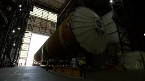 The orange core stage being moved into the large open doors of the Vehicle Assembly Building.