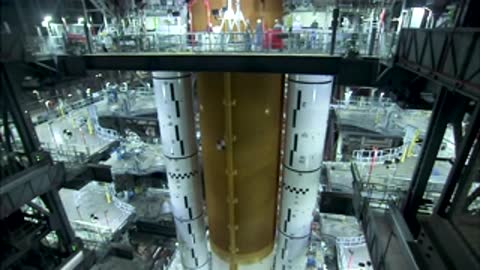View from a gantry bridge showing the tall orange core stage positioned between twin solid rocket boosters.