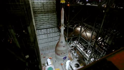 High-angle view of the tall white Orion spacecraft section positioned upright within the assembly scaffolding.