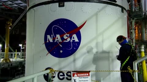 A technician stands near the large NASA logo painted on a rocket component.