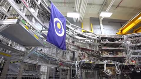 A purple flag hangs in a large industrial facility filled with electronics racks.