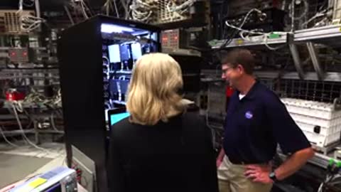 A woman in a dark suit talks to a man next to server racks.