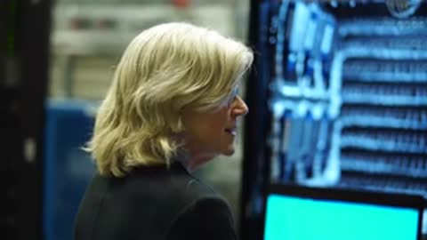 A woman in a dark suit speaks in front of blue lit server equipment.
