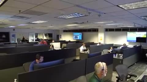 A wide shot of a control room with rows of operators sitting at desks.