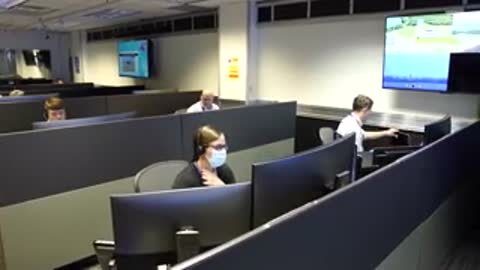 An operator wearing a face mask looks at monitors in a control room.