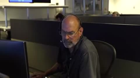 An operator with a headset looks at a computer screen in a control room.
