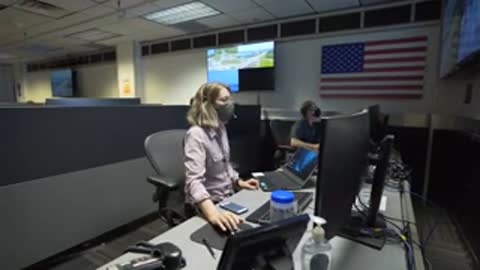 woman working at computer desk in office, control room, US flag on wall