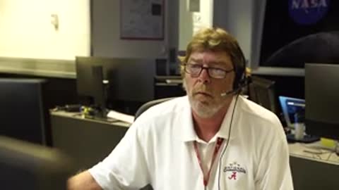 man with glasses wearing headset and white polo shirt inside mission control room
