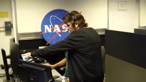 two people standing in front of NASA logo on wall inside control room