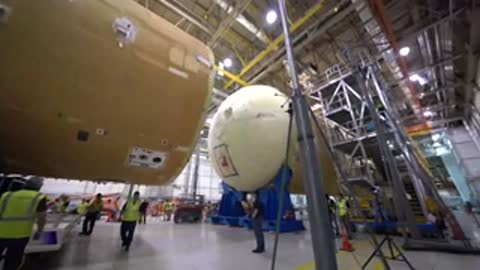 large rocket part being moved towards another section inside massive factory assembly building