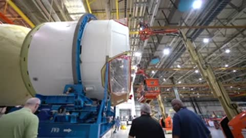 workers examining large cylindrical rocket component on transport assembly inside hangar