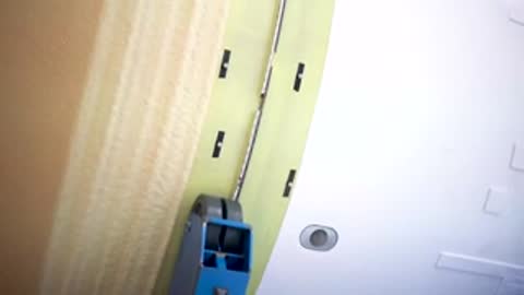 close up of automated tool sealing or applying tape along seam of rocket panel