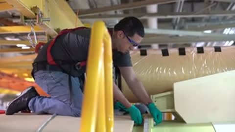 technician kneeling on floor of manufacturing facility working on large component panel