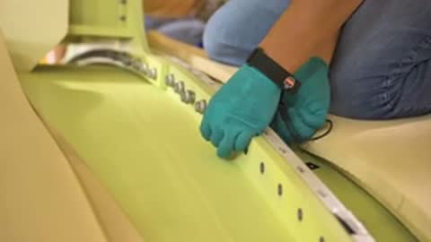 hands in green gloves securing components along edge of aerospace structure with tool