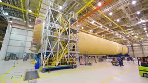 wide view of large aerospace facility interior with rocket stages and equipment on floor