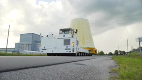 large conical rocket adapter being transported on flatbed vehicle outside facility building