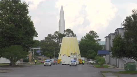 conical rocket adapter being transported on flatbed truck past buildings and trees outdoors
