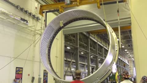 Engineers crane-lifting a large ring structure in a workshop.
