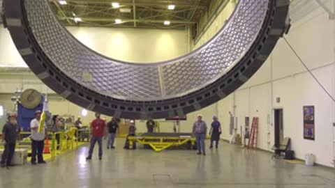 Engineers monitoring the crane-lifted ring structure in a spacious assembly hall.