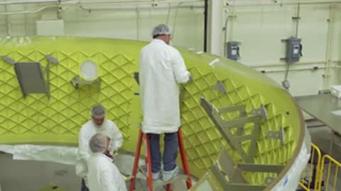 Technicians working on a curved metallic green panel framework in a workshop.