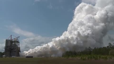 Exterior view of a rocket engine test firing, generating a large white cloud.