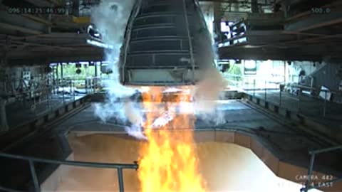 Interior view of a rocket engine firing bright orange flames in a test stand.