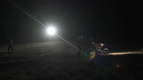 A bright light beam shines across a dark landscape with figures visible.