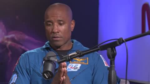 A man speaks in a studio setting against a blue backdrop with a microphone.
