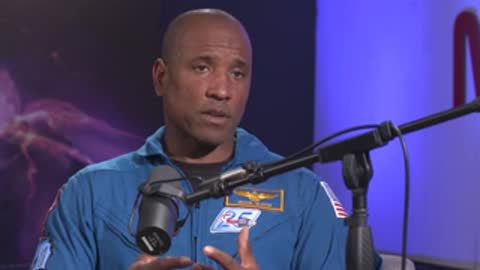 A man speaks in a studio setting against a blue backdrop with a microphone.