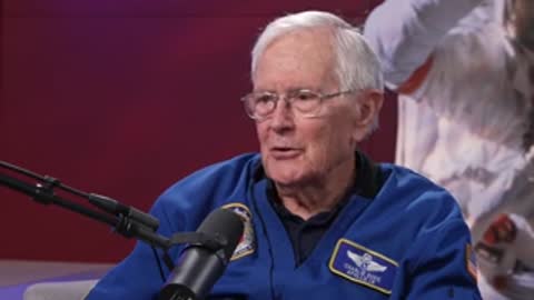 An older man in a blue jacket speaks in a studio setting.