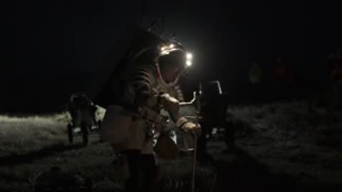 An astronaut in a space suit works with tools outdoors at night.