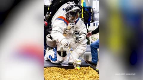 An astronaut in a space suit kneels and shovels material in a simulation container.