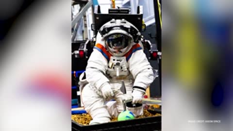 An astronaut in a space suit kneels inside a simulation container working.